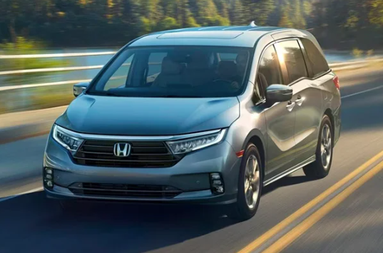 A silver 2024 Honda Odyssey driving down a road near a body of water near Indianapolis, Indiana