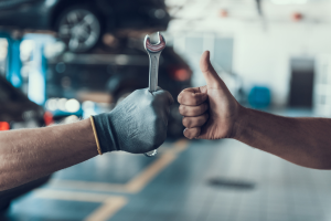 One person holding a thumbs-up sign, next to another person holding a wrench inside of a service center near Indianapolis, Indiana