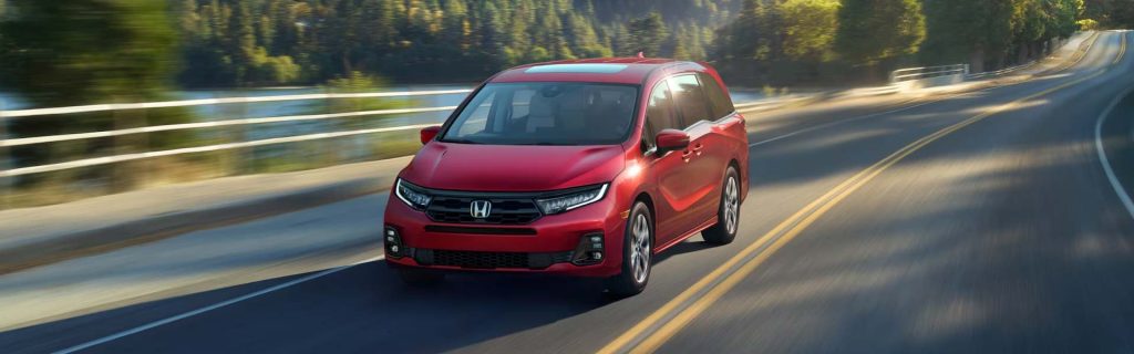 A red Honda Odyssey driving on a scenic road.
