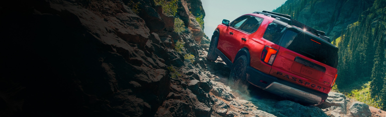 Red Honda Passport climbing a steep rocky trail, seen from behind