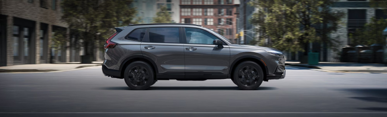 Grey Honda CR-V driving along a city street lined with brick buildings, shown in profile