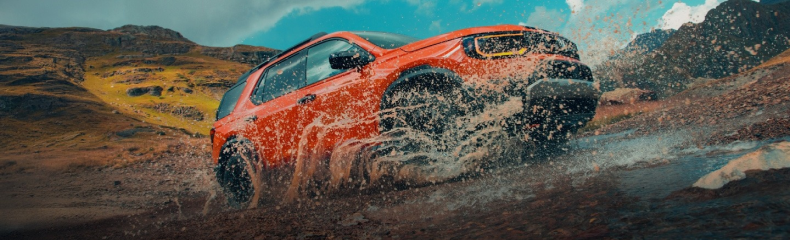 Orange Honda Passport TrailSport splashing through a rocky mountain stream