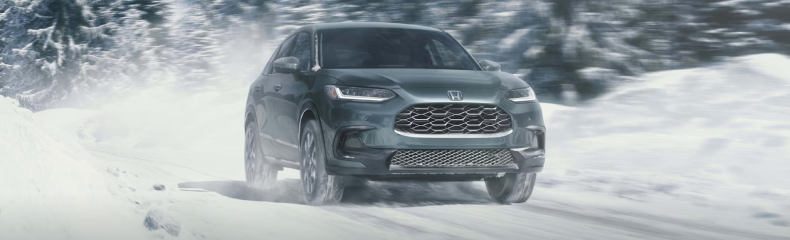Dark green Honda HR-V driving toward the camera on a snow-covered road through a wintry forest
