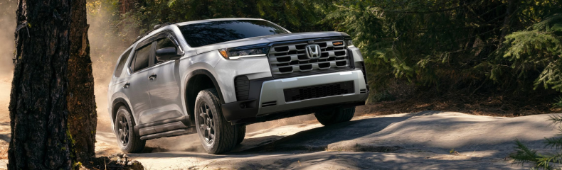 White Honda Passport TrailSport driving over rocks on a wooded trail