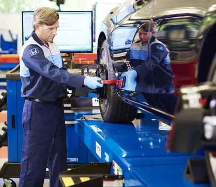 Honda technicians running a wheel alignment on a car raised on a service lift