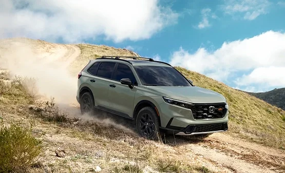 Green Honda CR-V TrailSport kicking up dust as it climbs a grassy hillside trail