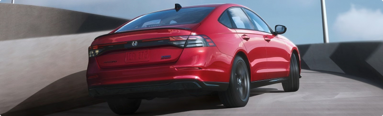 Red Honda sedan driving up a curved concrete ramp, seen from the rear quarter