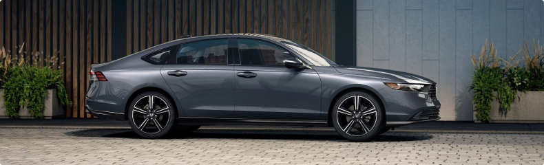 Grey Honda Accord parked in profile on a paved courtyard beside wood-slat and stone walls