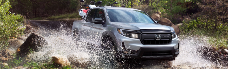 Silver Honda Ridgeline splashing through a rocky creek with dirt bikes in its bed