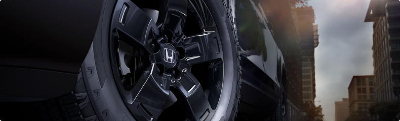 Close-up of a black Honda Ridgeline wheel and all-terrain tire on a city street