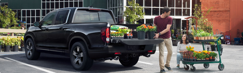 Couple loading potted flowers into the bed of a black Honda Ridgeline outside a garden center