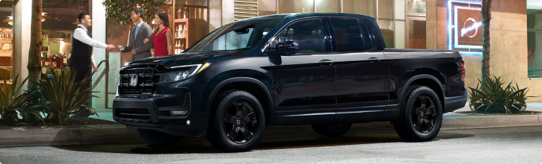Black Honda Ridgeline Black Edition parked outside a restaurant at night as a valet greets a couple