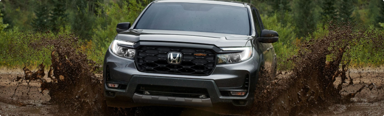 Grey Honda Ridgeline TrailSport driving head-on through deep mud