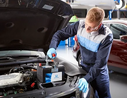 Honda technician testing a car battery under an open hood